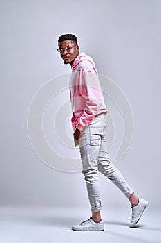 Full length portrait of a young african man wearing hoodie standing half-turn isolated over grey background