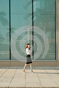 Full length portrait of young asian woman talking and walking with mobile phone