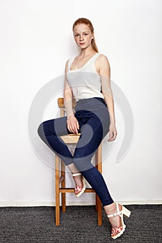 Full length portrait of young beautiful redhead beginner model woman in white t-shirt blue jeans practicing posing showing emotion