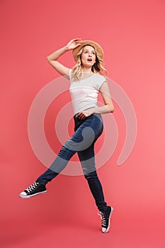 Full length portrait of young blond woman 20s wearing casual jeans and straw hat smiling and walking