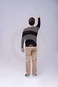 Full length portrait of a young casual man presenting something in the back isolated on gray background.