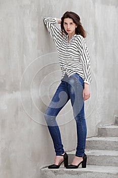 Full length portrait of young fashionable brunette woman practicing model posing outdoors against urban style background of grey c