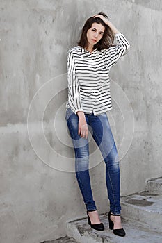 Full length portrait of young fashionable brunette woman practicing model posing outdoors against urban style background of grey c