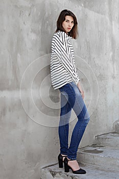 Full length portrait of young fashionable brunette woman practicing model posing outdoors against urban style background of grey c