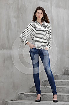 Full length portrait of young fashionable brunette woman practicing model posing outdoors against urban style background of grey c