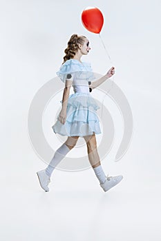 Full-length portrait of young girl wearing Halloween dress, costume of clown walking  over grey background