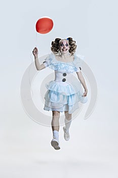 Full-length portrait of young girl wearing Halloween dress, costume of clown walking  over grey background