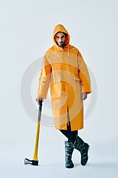 Full length portrait of young handsome man in bright raincoat holding big axe