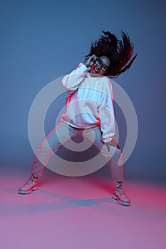 Full-length portrait of young happy dark skinned girl in hoodie jumping, dancing isolated on gradient blue-pink
