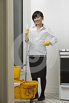 Full length portrait of young maidservant with mop and bucket photo