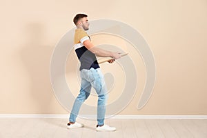 Full length portrait of young man carrying carton box near color wall.