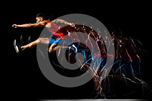 Full-length portrait of young man, professional track athlete, runner in a jump, training  over black background
