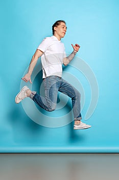 Full-length portrait of young man, student in casual style outfit jumping  on blue background. Human emotions