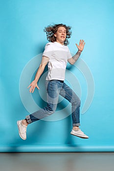 Full-length portrait of young man, student in casual style outfit jumping  on blue background. Human emotions