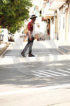 Full length portrait of young man walking outside with skateboard and bag