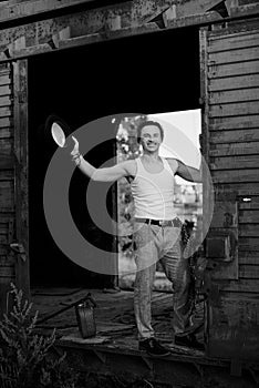 Full-length portrait of young man, wearing grey pants, white top, standing inside old railway carriage, leaning on doors. Black