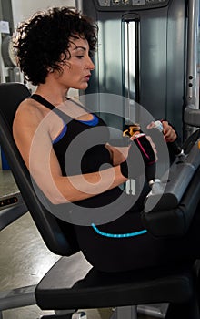 Full-length portrait of a young muscular girl with a blue bodice, use the Legg Press in the gym.