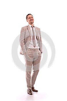 Full length portrait of a young positive man wearing  stylish beige suit with a tie.  He stands with his hands in his pockets and