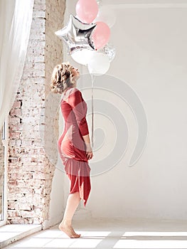 A full-length portrait of young pretty brunette woman with short curly hair, wearing red dress, doing dancing posing, holding pink