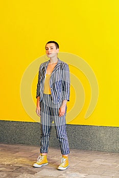 Full length portrait of young short hair beautiful woman in yellow shirt and casual style striped suit standing and looking at