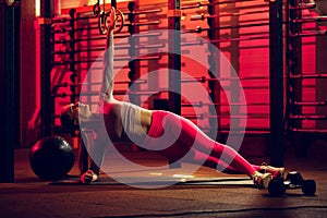 Full-length portrait of young sportive girl training, standing on side plank yoga pose isolated over gym background