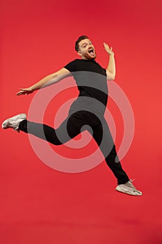 Full length portrait of young successfull high jumping man gesturing isolated on red studio background