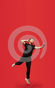Full length portrait of young successfull high jumping man gesturing isolated on red studio background