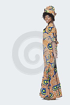 Full length portrait of young woman in African print attire standing over gray background