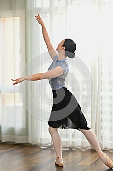 Full length portrait of young woman ballet dancer in pointe shoes practicing classic choreography near large window