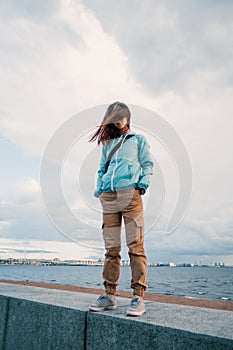 A full-length portrait of a young woman in a blue windbreaker in windy weather.