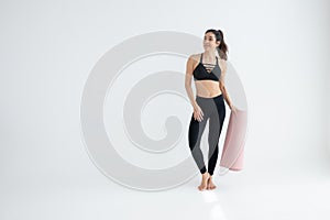 Full length portrait of a young woman holding yoga mat isolated