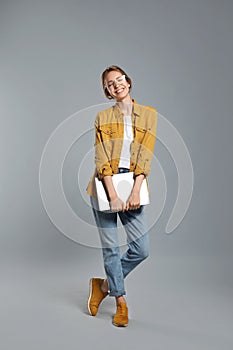 Full length portrait of young woman with laptop on grey background