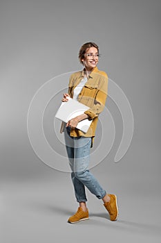 Full length portrait of young woman with laptop on grey background