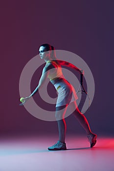 Full length portrait of young woman playing tennis isolated on dark background in neon. Healthy lifestyle, fitness