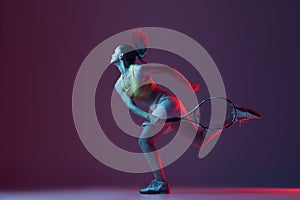 Full length portrait of young woman playing tennis isolated on dark background in neon. Healthy lifestyle, fitness