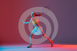 Full length portrait of young woman playing tennis isolated on dark background in neon. Healthy lifestyle, fitness