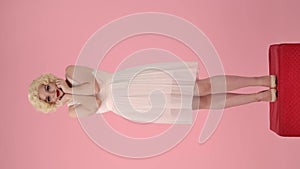 Full length portrait of young woman on red pedestal in studio on pink background. Woman in the image of Marilyn Monroe