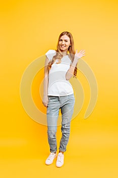 Full length, positive girl, shows a greeting gesture, on a yellow background