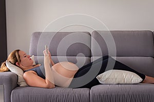 Full length of a pregnant woman lying on the sofa using her smartphone