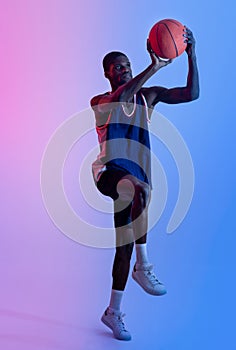 Full length of professional African American basketball player jumping and scoring ball in neon light