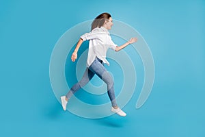 Full length profile photo of lady jumping high up running wear white shirt jeans shoes isolated blue color background