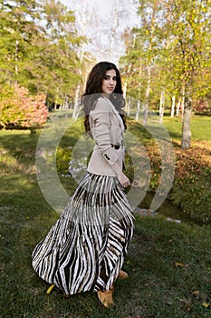 Full-length profile portrait of a beautiful brunette teen girl in elegant outfit, walking in the park.