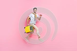 Full length profile portrait of cheerful nice man hold suitcase jump rush empty space isolated on pink color background