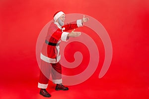 Full length profile shot of elderly man with gray beard wearing santa claus costume reaching hands