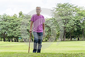 Full length profile shot of a senior man walking with a cane in a park. Elderly old man with walking stick standing in a public