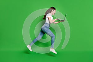 Full length profile side photo of crazy girl jump run use laptop wear t-shirt denim isolated over green color background