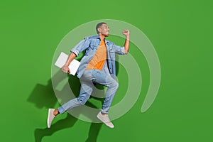 Full length profile side photo of good mood young man running with laptop isolated on green color background