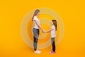 Full length profile side photo of lovely mommy with her kid having long haircut holding hands isolated over yellow