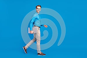 Full length profile side photo of young business man happy positive smile go walk hold laptop isolated over blue color