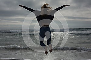 Full length rear view of a woman jumping at beach